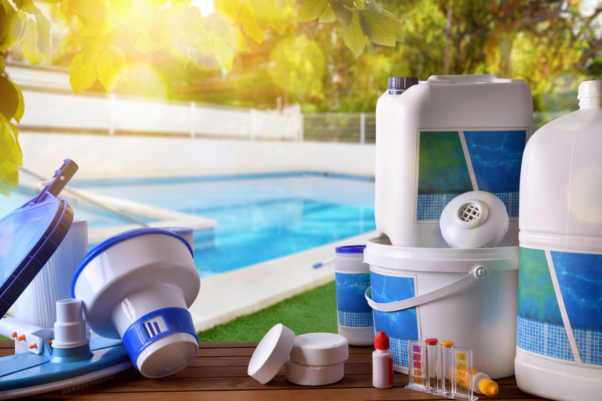 Swimming pool service and equipment with chemical cleaning products and tools on wood table and pool background. Horizontal composition. Front view