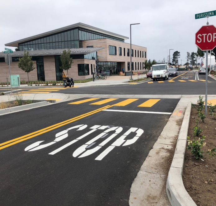 Street with fresh-painted cross walk and the word "stop" on the street; next to the street is a green infrastructure element with dirt and plants between concrete to capture and clean stormwater runoff