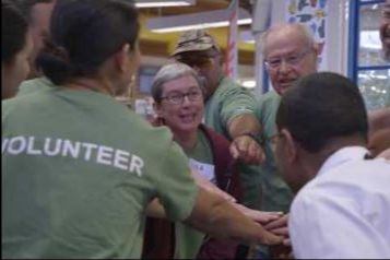 group of people putting their hands into the center; green shirt that says volunteer